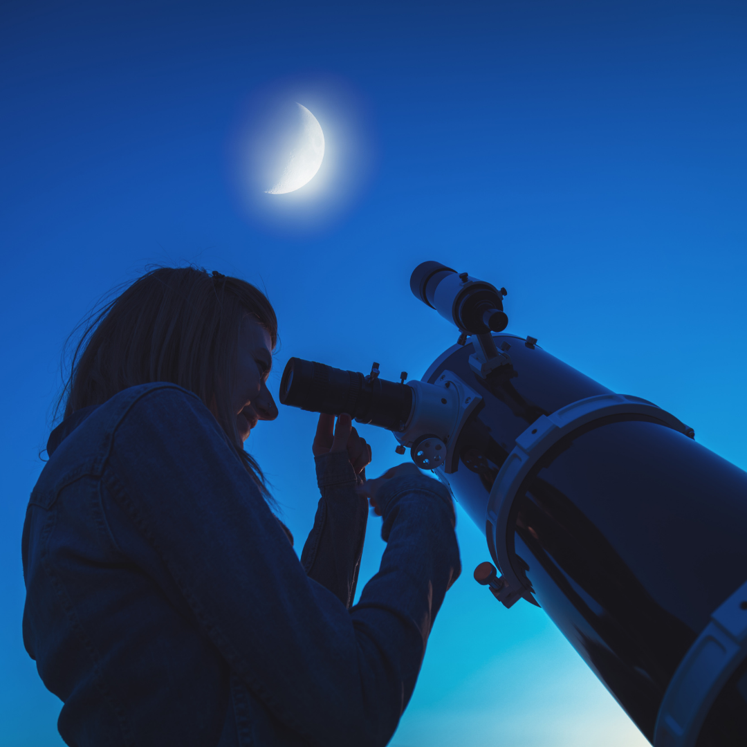 Photo of a young woman at a telescope pointed at the moon